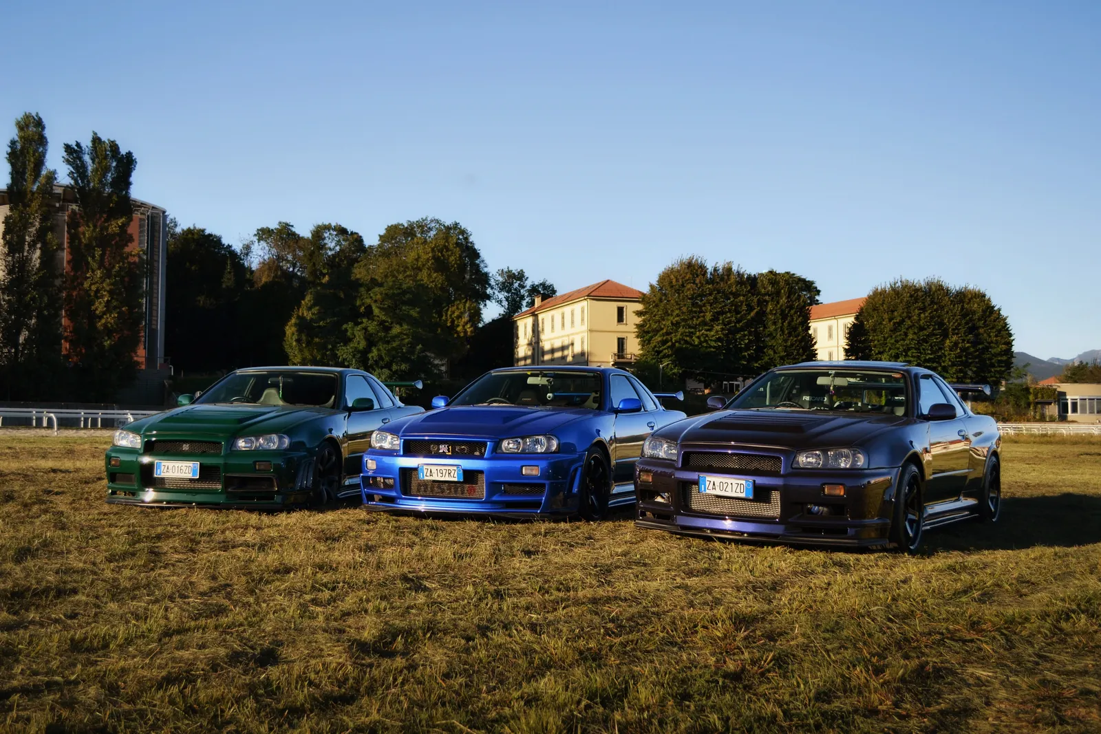 Three Nissan Skyline GT-R in green, blue and purple parked on a field