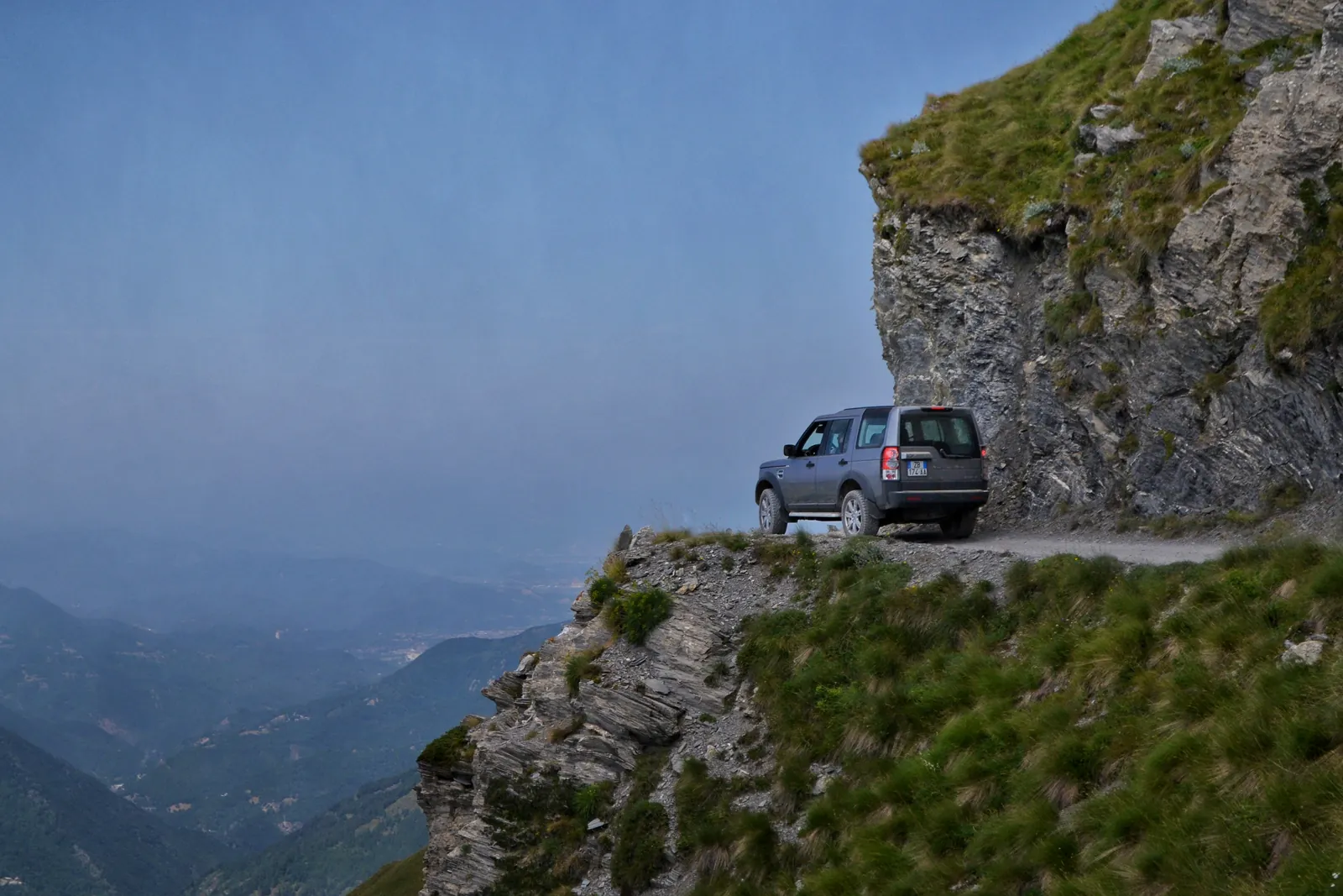 Off-road SUV on a cliff-edge mountain road above a valley