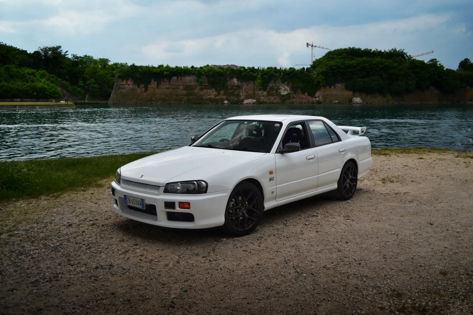 White Nissan Skyline sedan parked beside a lake