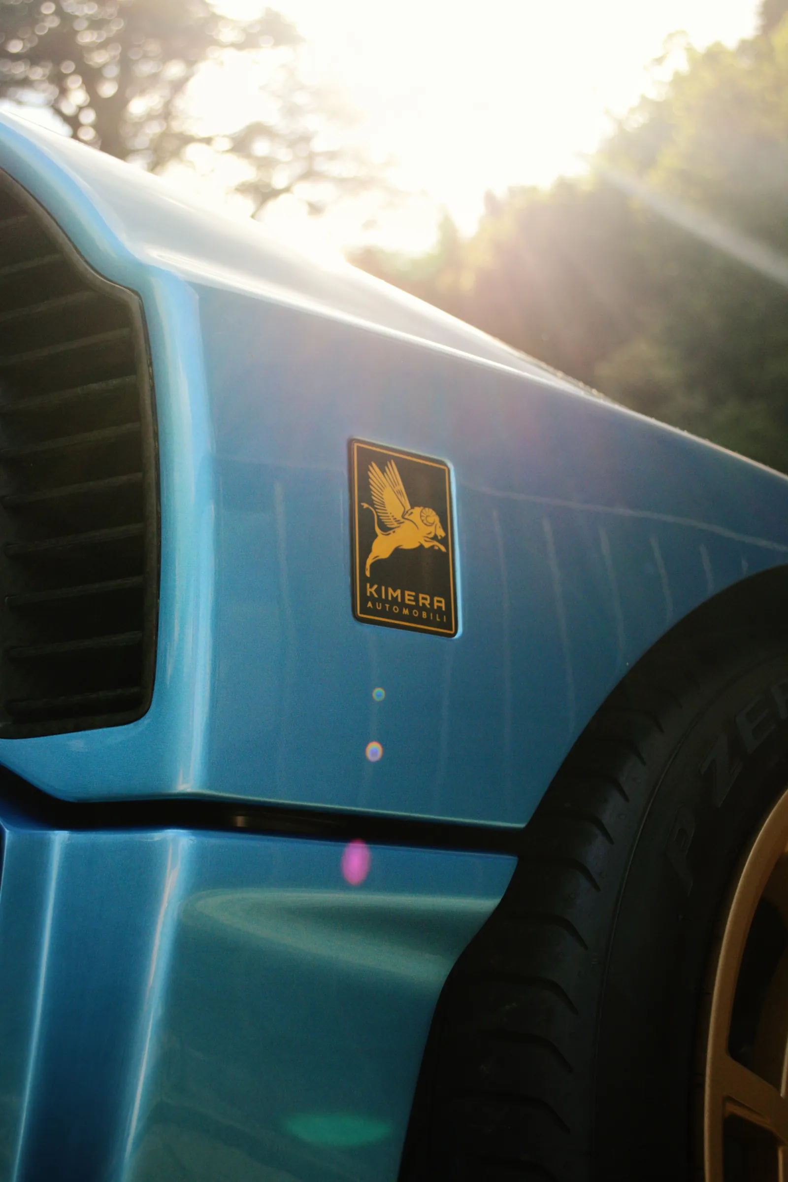 Detail of a blue Kimera sports car with sun flare and gold wheel