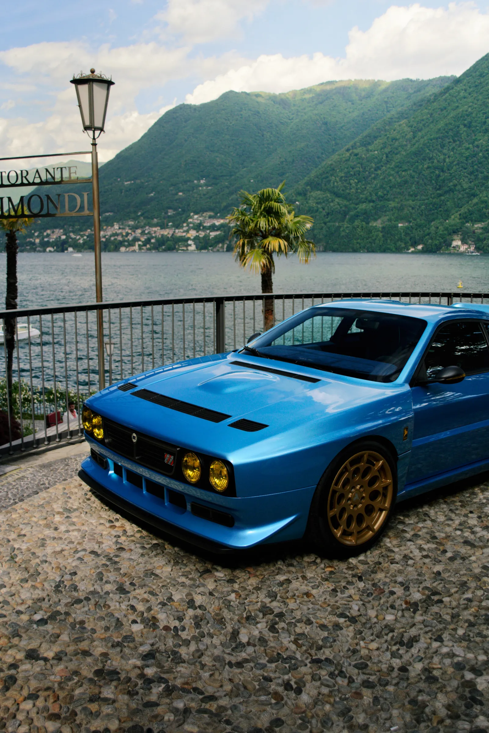 Blue retro sports car with gold wheels beside a lake and mountains