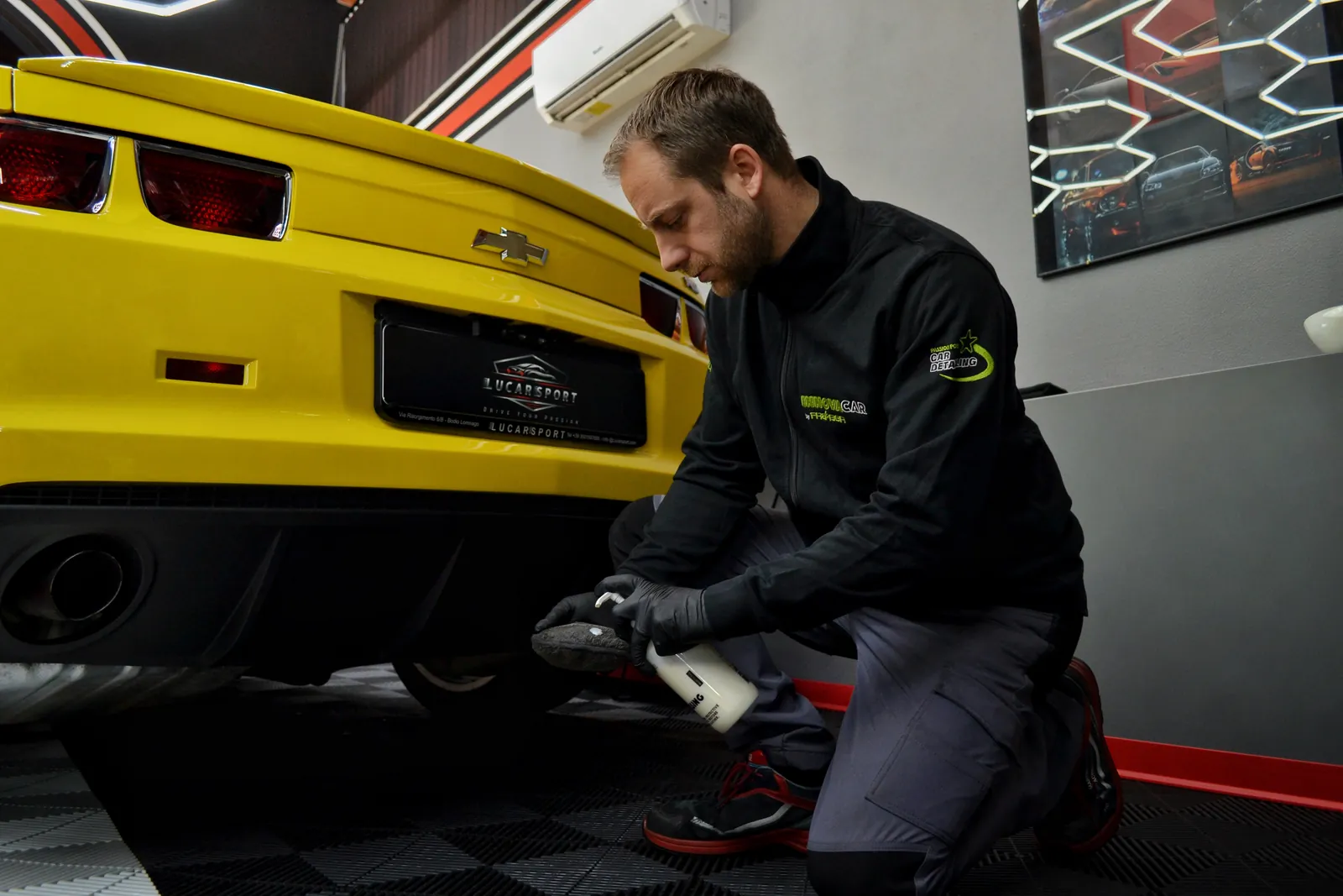 Detailer working on the rear of a yellow Chevrolet Camaro in a studio
