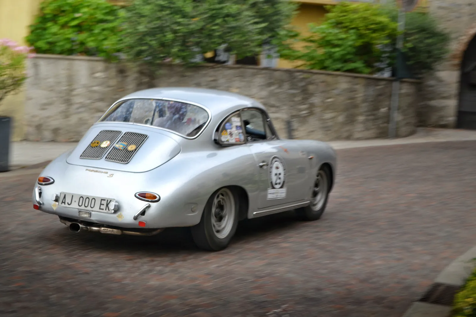 Silver vintage Porsche 356 driving through a village in a classic rally